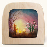 Toverlux magic lamp with a kinding spring snowdrop gnome silhouette by artist Vogel Geluk. A watercolour style illustration of a gnome carrying a lit candle walking towards a bunch of snowdrops. A range of Toverlux silhouettes, lamps and accessories are available at Babipur.