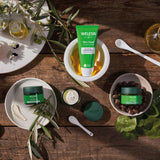A collection of Weleda skin care products sitting inside white bowls on a wooden table. Image showing the cleansing balm and the night  and day nourishing creams. These are all available at Babipur.