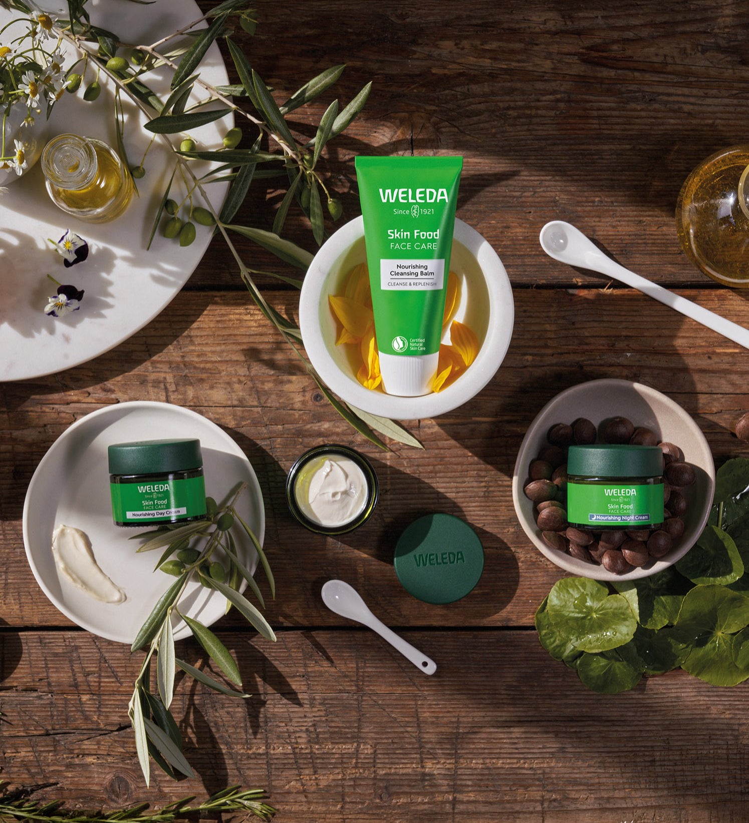 A collection of Weleda skin care products sitting inside white bowls on a wooden table. Image showing the cleansing balm and the night  and day nourishing creams. These are all available at Babipur.