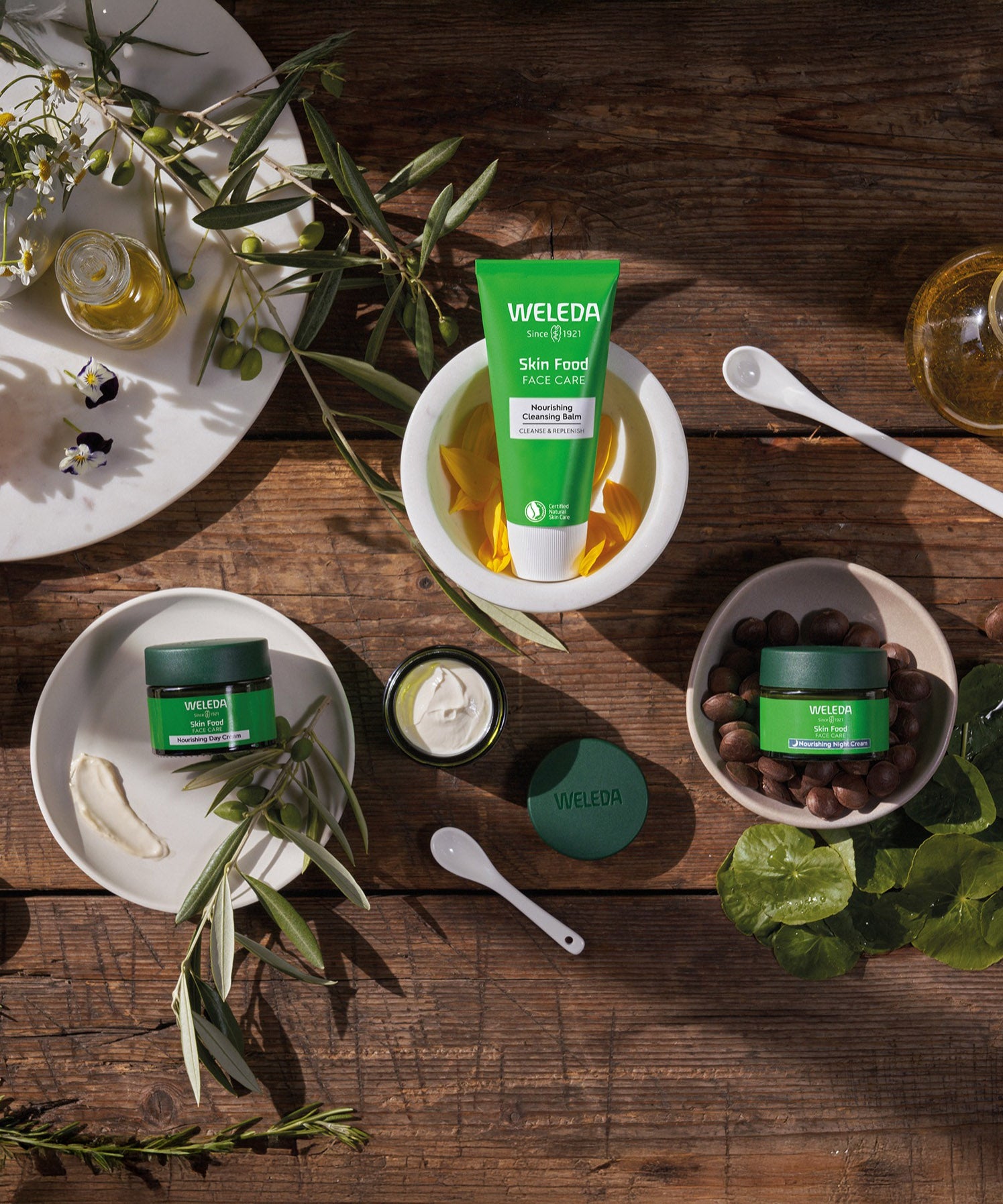 A collection of Weleda skin care products sitting inside white bowls on a wooden table. Image showing the cleansing balm and the night  and day nourishing creams. These are all available at Babipur.