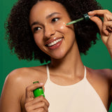 A woman applying the Weleda skin food super serum on her face and showing the  glass bottle and pipette. Weleda have a range of luxurious, natural skin care items available at Babipur.