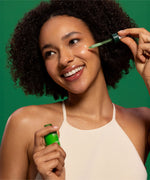 A woman applying the Weleda skin food super serum on her face and showing the  glass bottle and pipette. Weleda have a range of luxurious, natural skin care items available at Babipur.