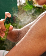 A close up of the Weleda skin food ultra light dry oil bottle sprayed on a woman's arm. This dry oil is available at Babipur.
