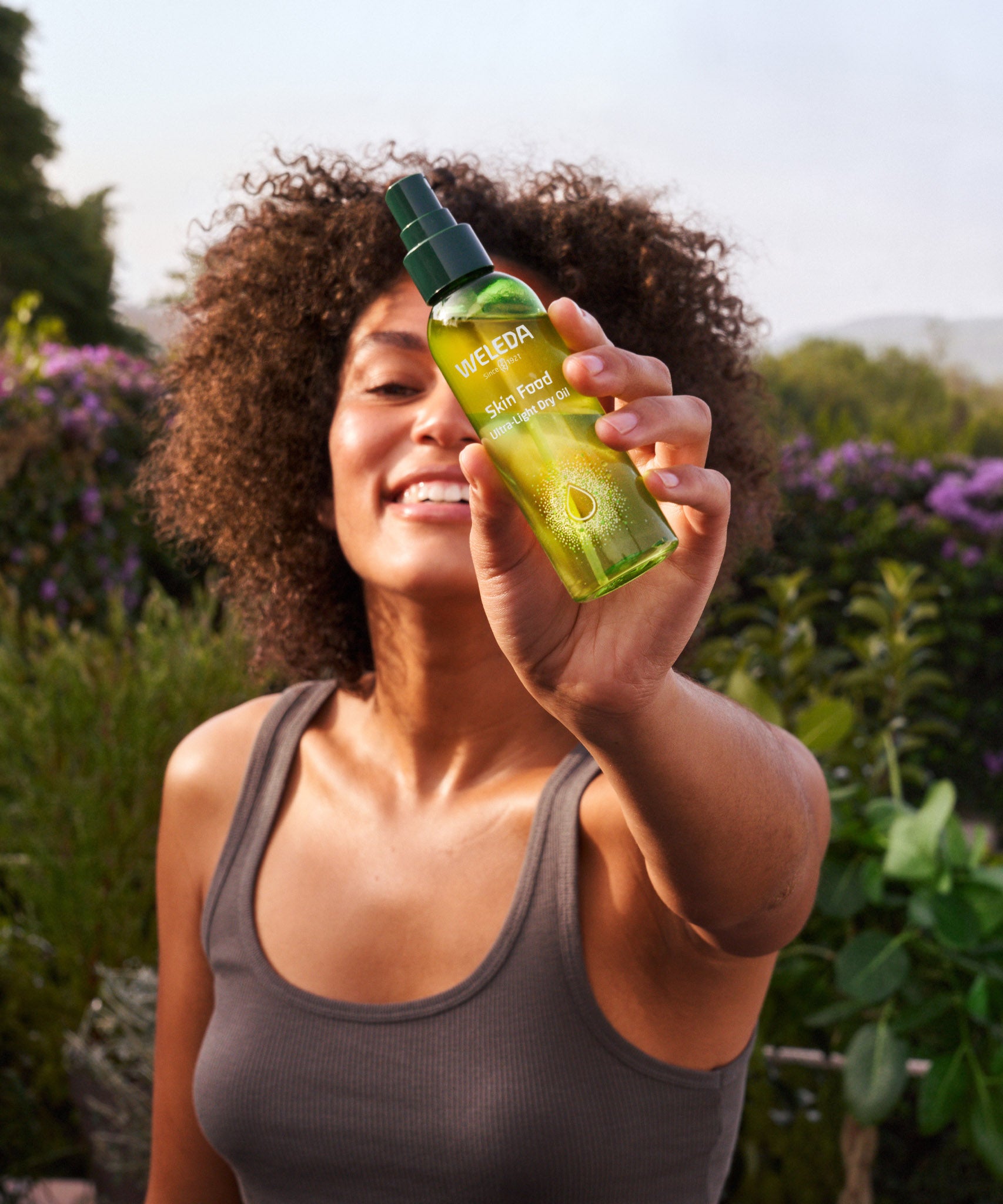 A woman holding the the Weleda skin food ultra light dry oil. This bottle is available at Babipur.