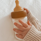 Baby wearing a cream jumper with a Hevea Glass Baby Bottle