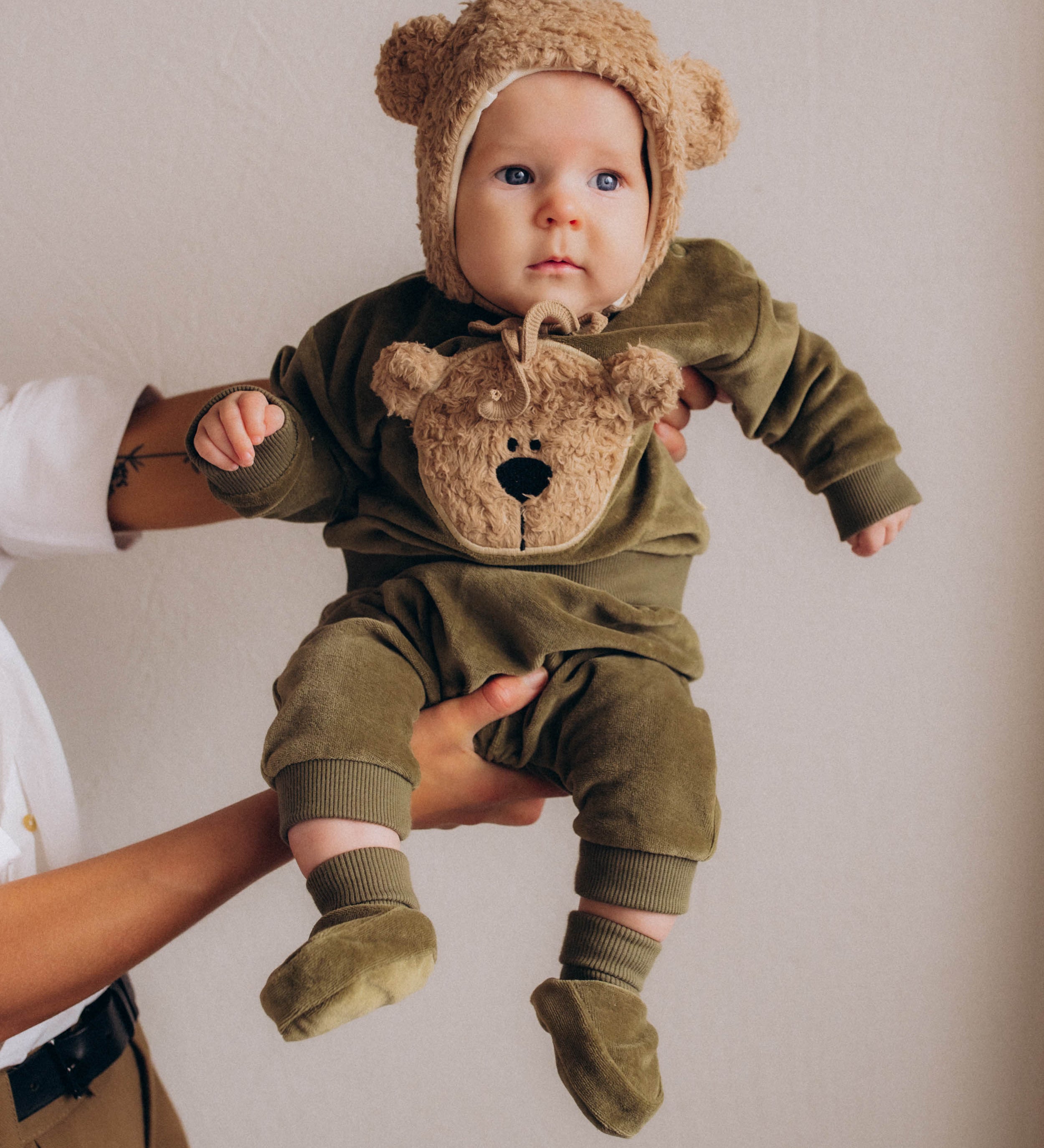 A baby wearing the Wooly Organic embroidered sweater in tea leaf /savannah available at Babipur showing the popper fastener detail
