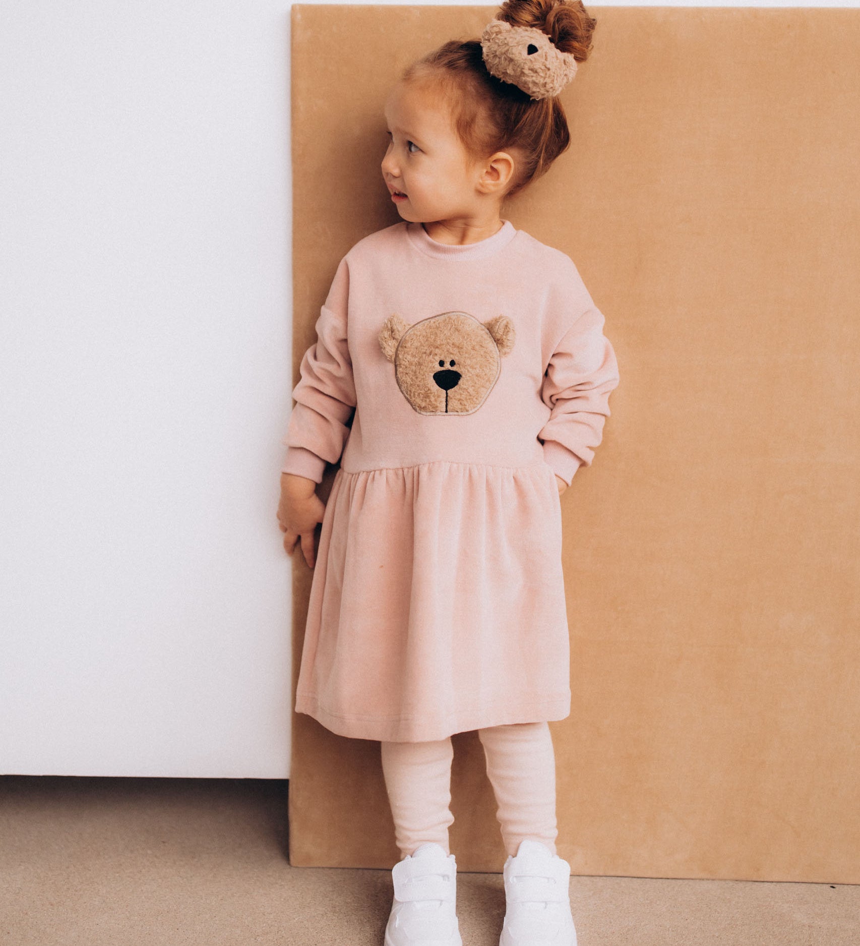 A child wearing the Wooly Organic velour scrunchy with a fluffy teddy on their head. Scrunchy available at Babipur.
