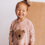 A child wearing the Wooly Organic velour scrunchy in cream with a fluffy teddy on their head. Scrunchy available at Babipur.