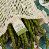 A close up of the A Slice Of Green recycled cotton small mesh produce bag showing the mesh detail and the bunch of asparagus inside to show scale. Features a total carry weight limit tag on the inside.