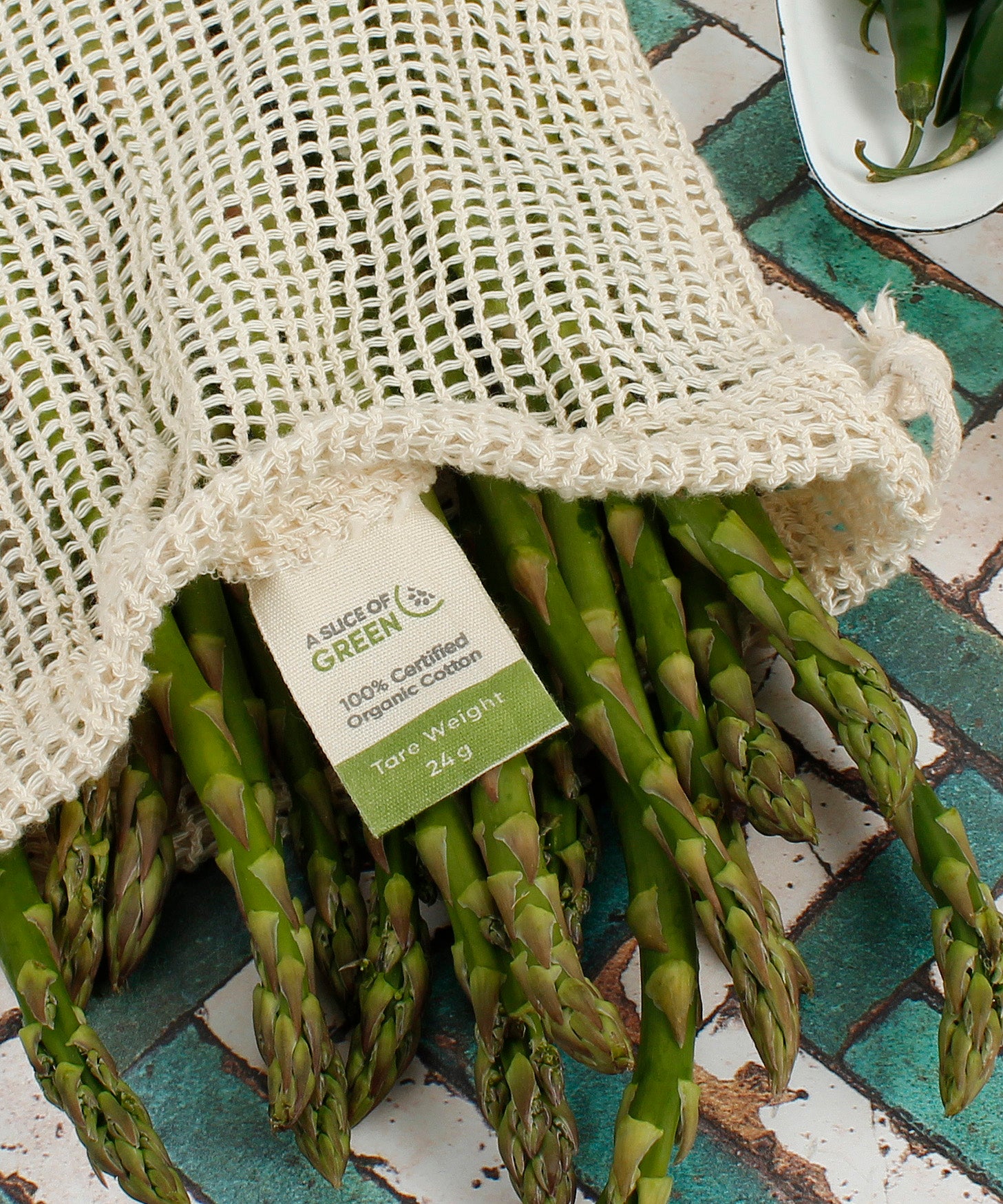 A close up of the A Slice Of Green recycled cotton small mesh produce bag showing the mesh detail and the bunch of asparagus inside to show scale. Features a total carry weight limit tag on the inside.