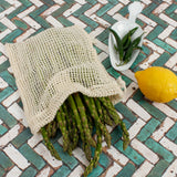 A Slice Of Green small mesh produce bag made from recycled cotton showing a bunch of asparagus inside next a lemon and chillies showing scale.