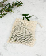A Slice Of Green small mesh produce bag laid flat on a stone surface. A recycled cotton bag showing a bunch of green chillies inside.