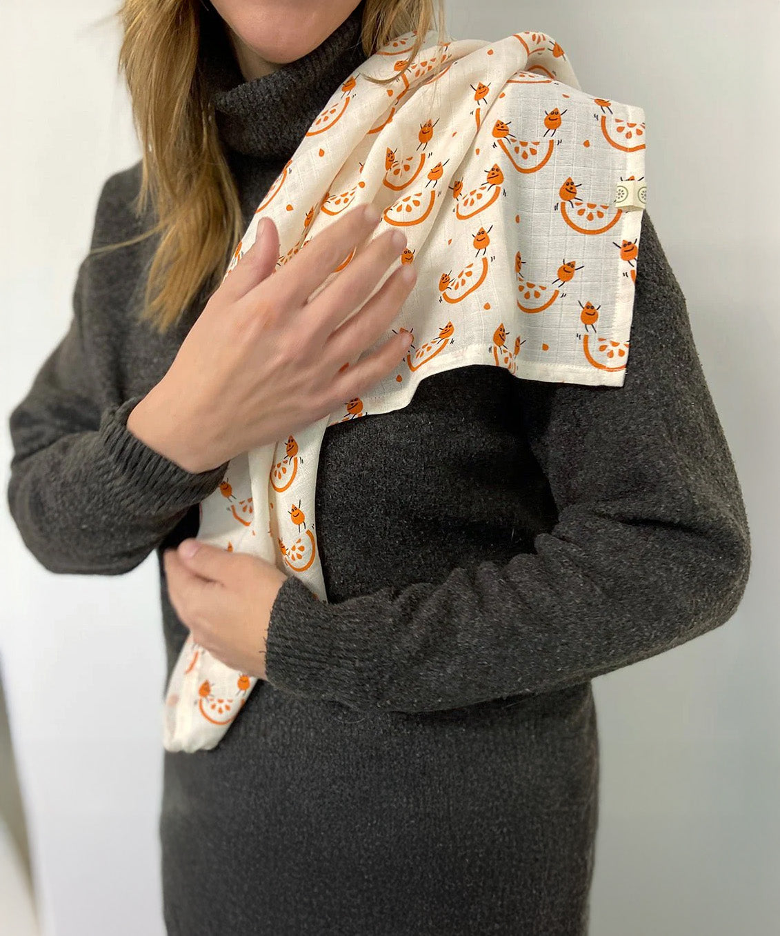 An adult with the organic cotton A Slice Of Green muslin cloth in orange design over the shoulder showing the scale of the cloth