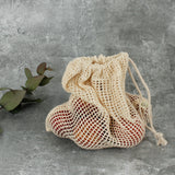 A Slice Of Green small mesh produce bag standing up on a stone surface with  a bunch of red apples inside to show scale