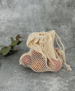 A Slice Of Green small mesh produce bag standing up on a stone surface with  a bunch of red apples inside to show scale