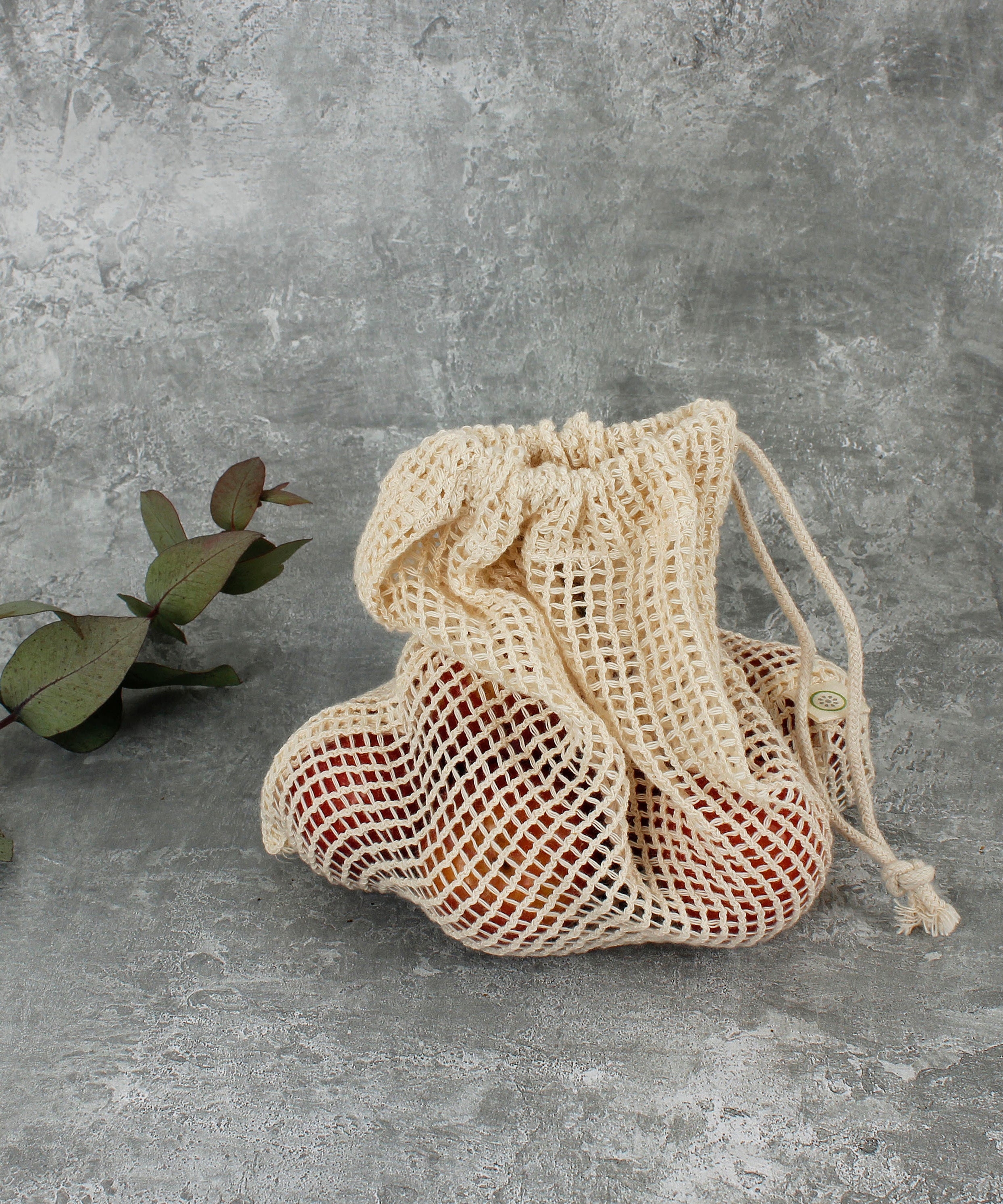 A Slice Of Green small mesh produce bag standing up on a stone surface with  a bunch of red apples inside to show scale