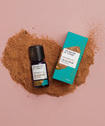 Atlas Cedar pure essential oil in a blue glass bottle next to a decorative blue cardboard box on a background of brown wood dust..