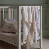 The cloths from the Avery Row Wildflower Baby Muslin Squares in a Set of 3 draped on the side of a cot bed. One cloth is plain white, one has delicate pink flowers and one has an all over floral wildflower design. Avery Row have a collection of stylish nursery and baby essentials available at Babipur.