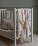 The cloths from the Avery Row Wildflower Baby Muslin Squares in a Set of 3 draped on the side of a cot bed. One cloth is plain white, one has delicate pink flowers and one has an all over floral wildflower design. Avery Row have a collection of stylish nursery and baby essentials available at Babipur.