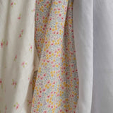 A close up of the design on the cloths from the Avery Row Wildflower Baby Muslin Squares in a Set of 3. One cloth is plain white, one has delicate pink flowers and one has an all over floral wildflower design. Avery Row have a collection of stylish nursery and baby essentials available at Babipur.