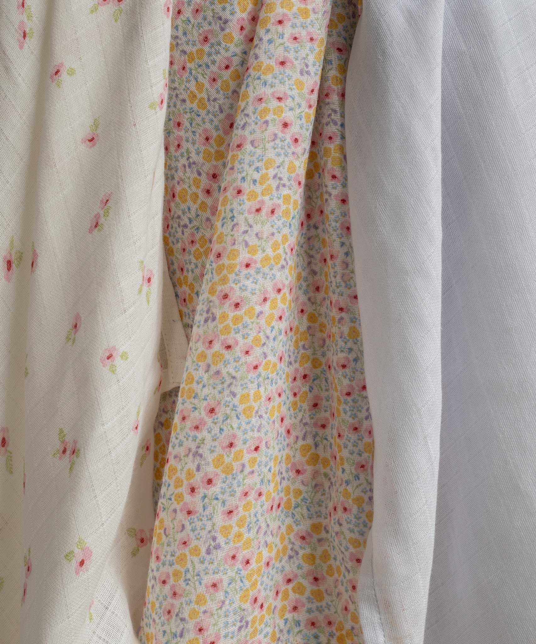 A close up of the design on the cloths from the Avery Row Wildflower Baby Muslin Squares in a Set of 3. One cloth is plain white, one has delicate pink flowers and one has an all over floral wildflower design. Avery Row have a collection of stylish nursery and baby essentials available at Babipur.