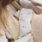 A close up of a baby in a baby carrier, a woman can be seen holding a swaddle that is covering the baby  Avery Row Coastline baby Muslin Swaddle. The swaddle features a delicate coastline print that has corals and little blue fish. Avery Row have a collection of stylish nursery and baby essentials available at Babipur.