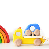 Bajo children's wooden tow truck toy on a white table next to a Grimms mini rainbow toy