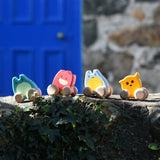 Four Bajo push along wooden ghost toys paced on a stone wall outdoors. Toe toy has a yellow painted body and natural wooden wheels. These heirloom quality toys by Bajo are part of a wide range of wooden toys available here at Babipur.