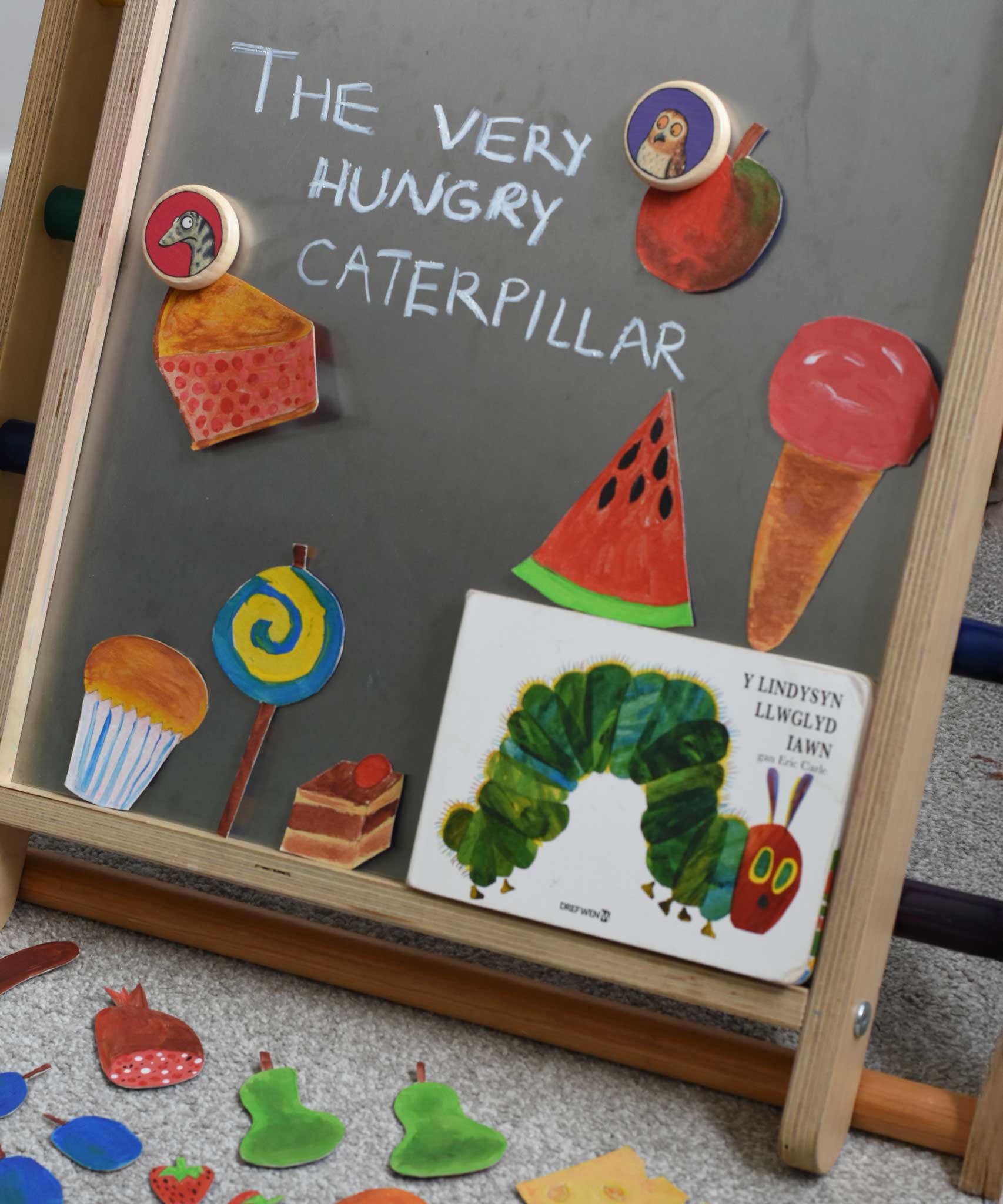 A snake and owl Bajo magnet placed on the Triclimb biri board with hand drawn food featured in the very hungry caterpillar book. These magnets are part of a range of Bajo wooden toys available at Babipur.