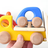 Bajo children's wooden tow truck toy on a white table next to a Grimms mini rainbow toy