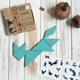 A blue coloured Bajo Tangram puzzle placed on a white wooden surface. The pieces from the Tangram puzzle have been placed in the shape of a fox. The accompanying ideas booklet can be seen open with the cardboard box placed besides it. These heirloom quality toys by Bajo are part of a wide range of wooden toys available here at Babipur.