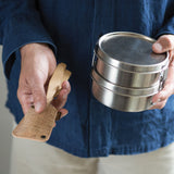 A person holding the Bambu Bamboo Utensil Travel Set with Cork Fabric Pouch with a metal food tin