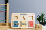 Big Future Toys wooden latch board on its stand on a wooden table next to an abacus in front of a grey wall