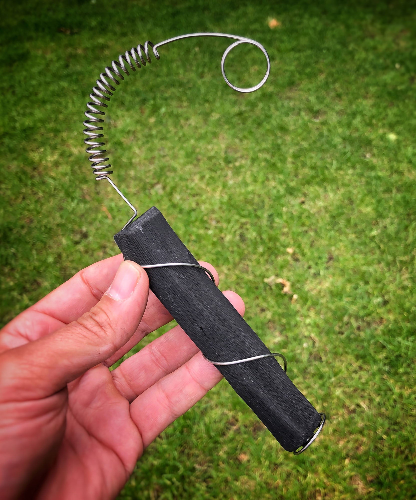 A close up of an adult hand holding the Black + Blum active charcoal water filter with metal coil showing the size