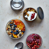 A top down view of the Black + Blum leakproof microwave safe glass lunchbowl showing different cereals inside the glass bowl and showing the silicone lid detail.