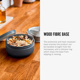 An open Black+Blum Leakproof Microwave Safe Glass Lunch Bowl filled with food. The text along side reads, wood fibre base. The protective and heat resistant base ensures the product can be handled straight from the microwave, with a silicone ring which stops the base from sipping or moving.