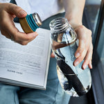 A close up of a person taking the lid off the Black+Blum Glass Water Bottle With Active Charcoal Filter & Coil.