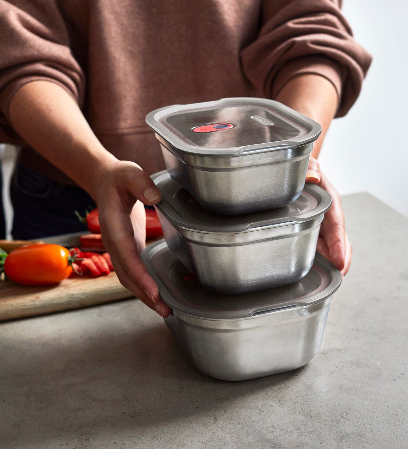 A adult standing by a stone worktop with the 3 different sized Black + Blum stainless steel lunchbox stacked on top of eachother