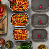 A top down view of the 3 sized Black + Blum stainless steel lunch boxes next to eachother on a stone worktop with food inside