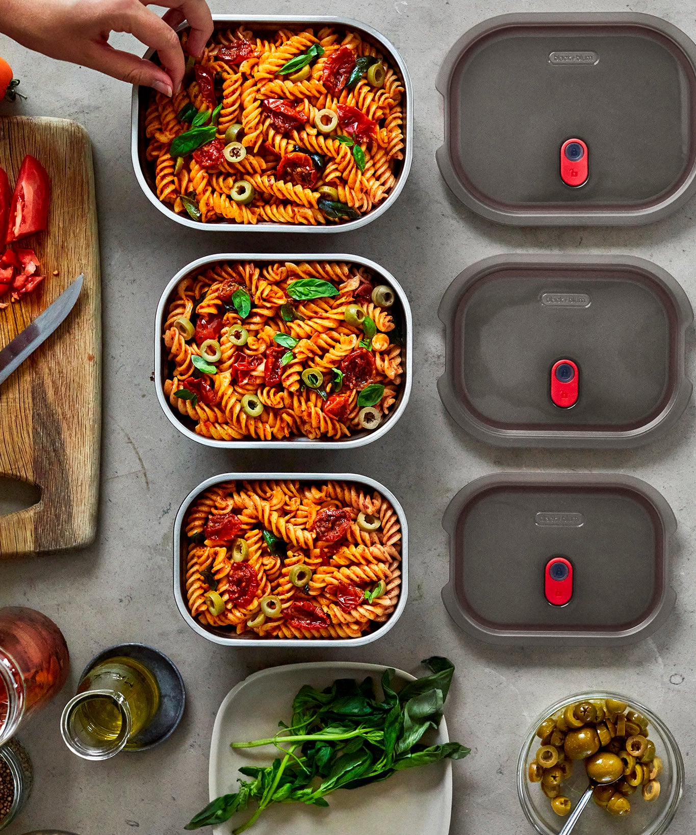 A top down view of the 3 sized Black + Blum stainless steel lunch boxes next to eachother on a stone worktop with food inside