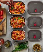 A top down view of the 3 sized Black + Blum stainless steel lunch boxes next to eachother on a stone worktop with food inside