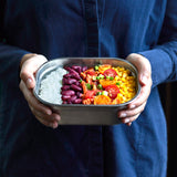 A adult standing and holding the Black + Blum stainless steel lunchbox with food inside.