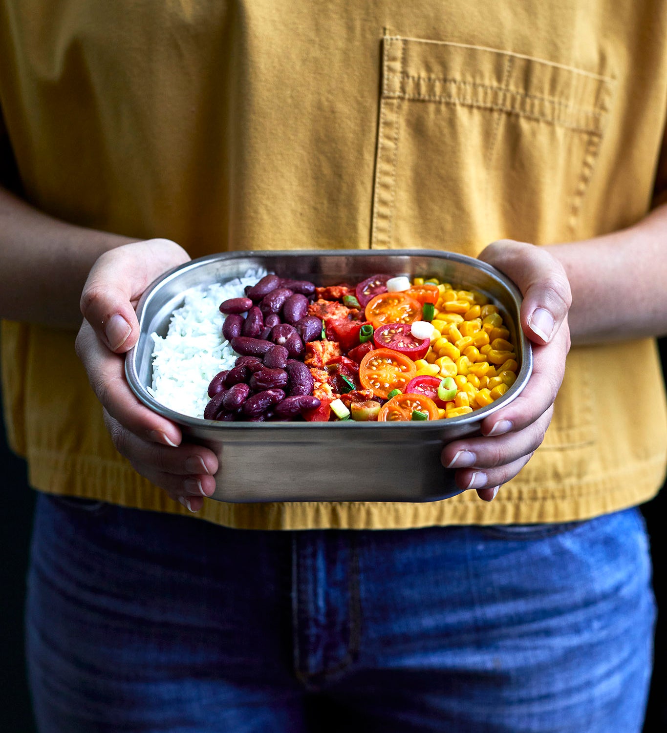 A adult standing and holding the 600ml Black + Blum stainless steel lunchbox with food inside.