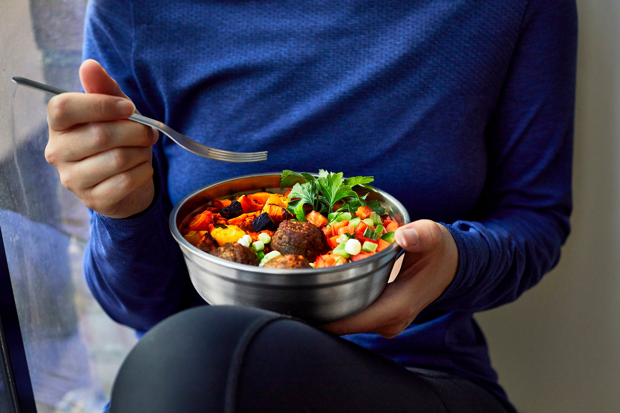 A close up of an adult eating from  a small Black + Blum stainless steel bowl