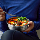 A close up of an adult eating from  a small Black + Blum stainless steel bowl