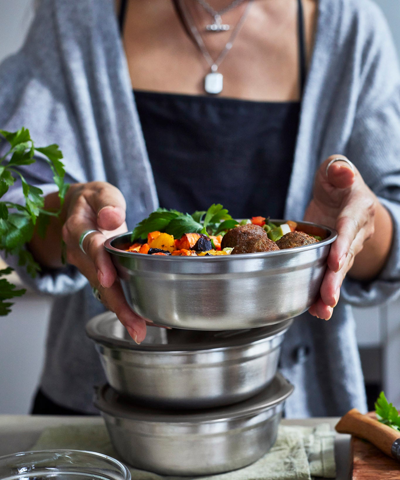 An adult standing over a kitchen worktop with different sized Black + Blum stainless steel bowls stacked on top of eachother