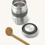 A close up of the Black + Blum insulated stainless steel food flask with wooden spoon showing the olive green elastic strap and lid detail