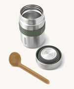 A close up of the Black + Blum insulated stainless steel food flask with wooden spoon showing the olive green elastic strap and lid detail