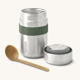 A close up of the Black + Blum insulated stainless steel food flask in olive showing the wooden spoon and lid resting next to the flask