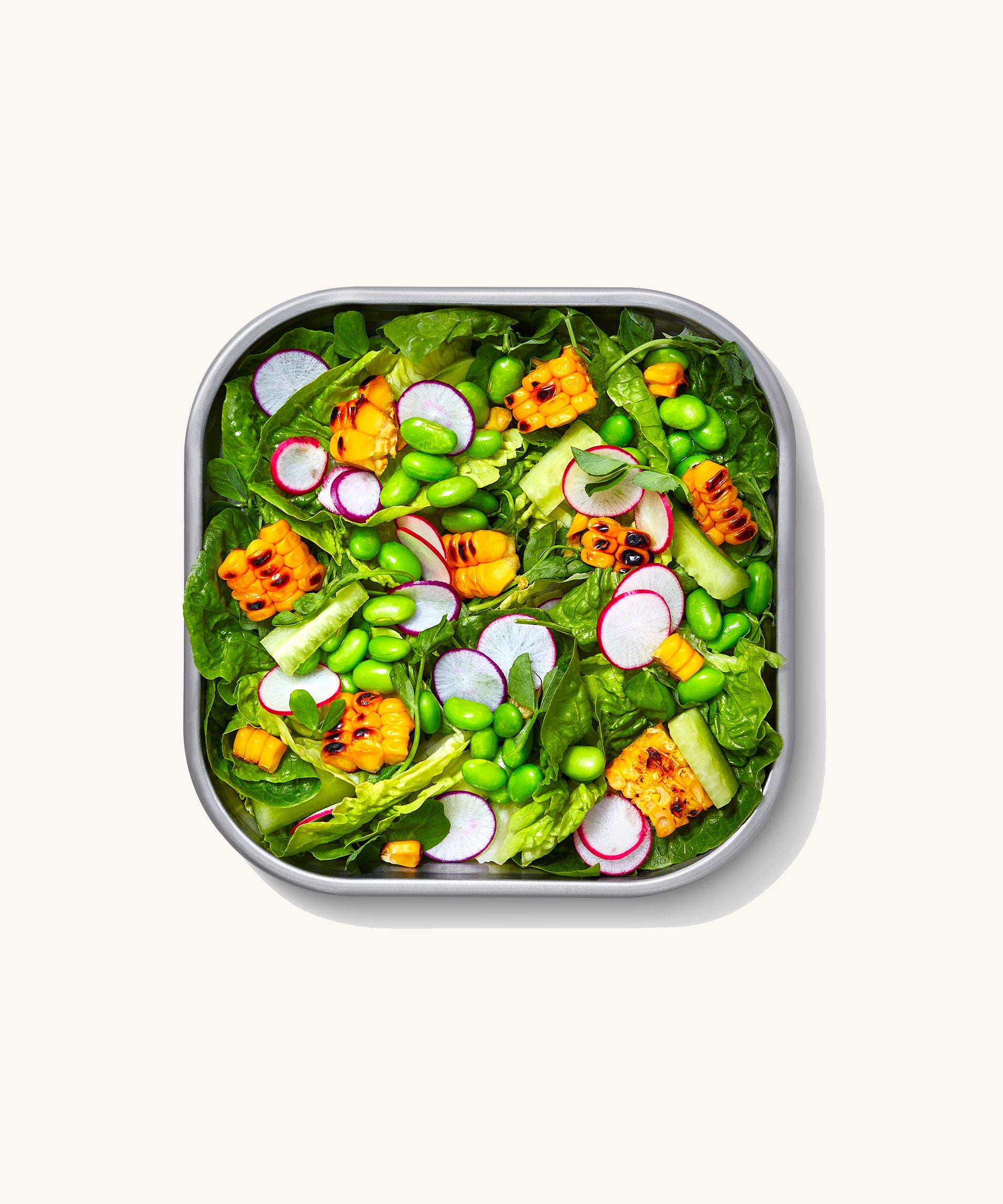 A close up of a Black + Blum square stainless steel leakproof microwave safe lunchbox showing a salad dish inside the lunchbox